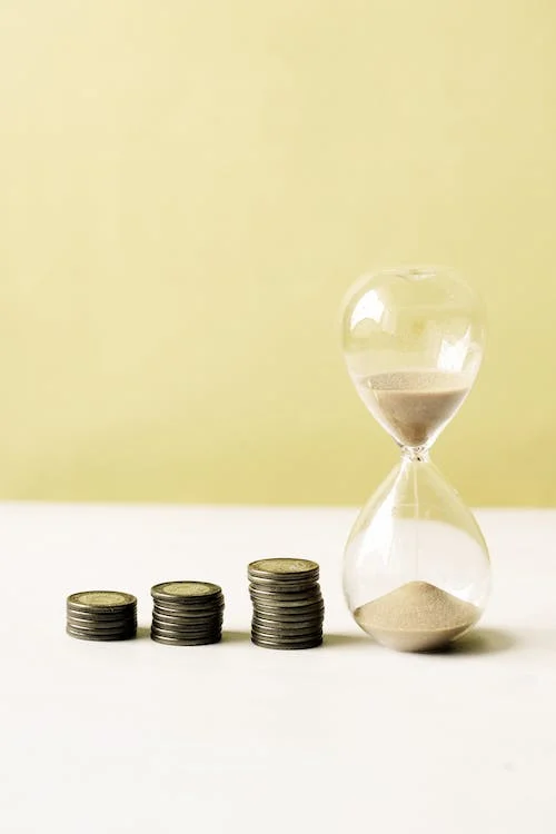 Image of an hourglass with coins beside it, symbolizing the careful and timely management of resources by Reignmakers. This image represents the diligent approach and personalized attention to the optimization of clients' financial stability and security through precise and comprehensive financial and tax planning services, which include efficient wealth transfer and tax-advantaged investment strategies